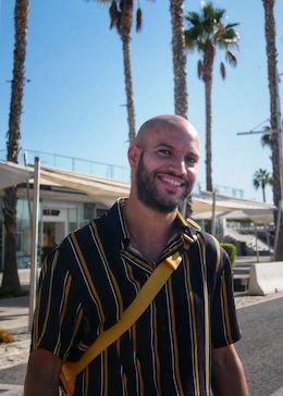 Adil wearing a sriped shirt and posing in front of palm trees 