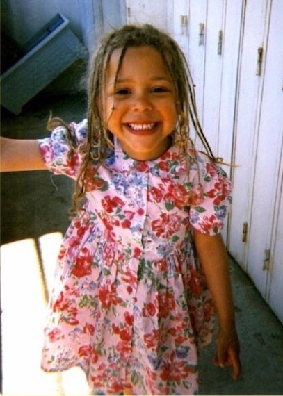 A young Tiffany Rousseau in a pink flowery dress smiling